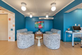 Two grey patterned chairs are in front of a blue wall with a painting and a computer desk.